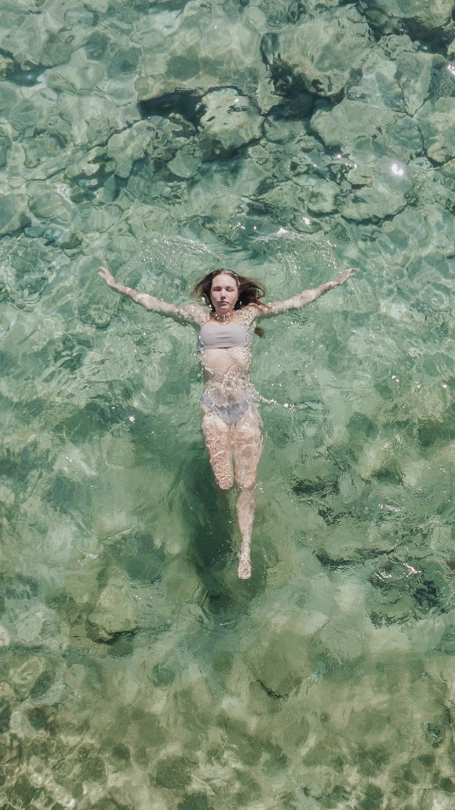 Woman floating in crystal clear water wearing Kirra swim top in the colour Taupe.