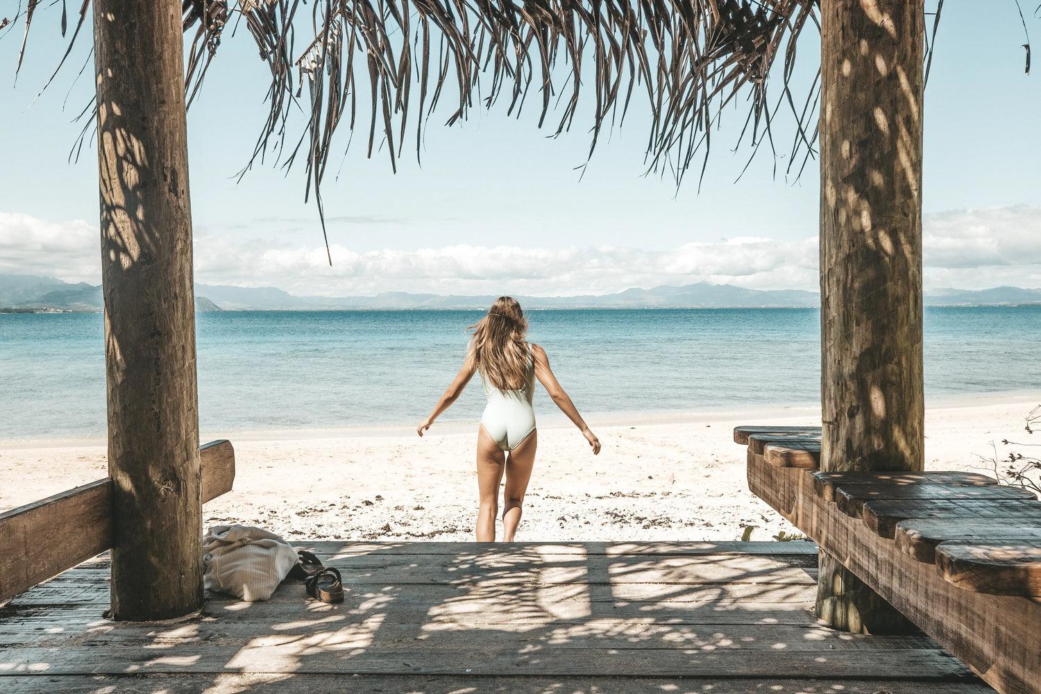 Woman on a tropical beach, running towards the water wearing the Talia one piece in the colour Moss, showcasing the elegant framed back.