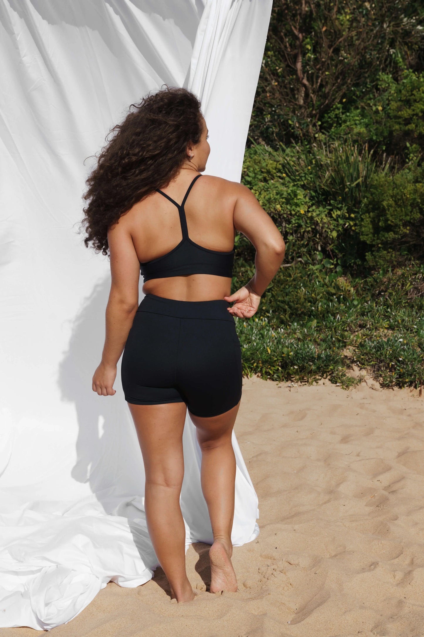 Model at the beach facing the back wearing our Inala Crop and Allawah Short in Black